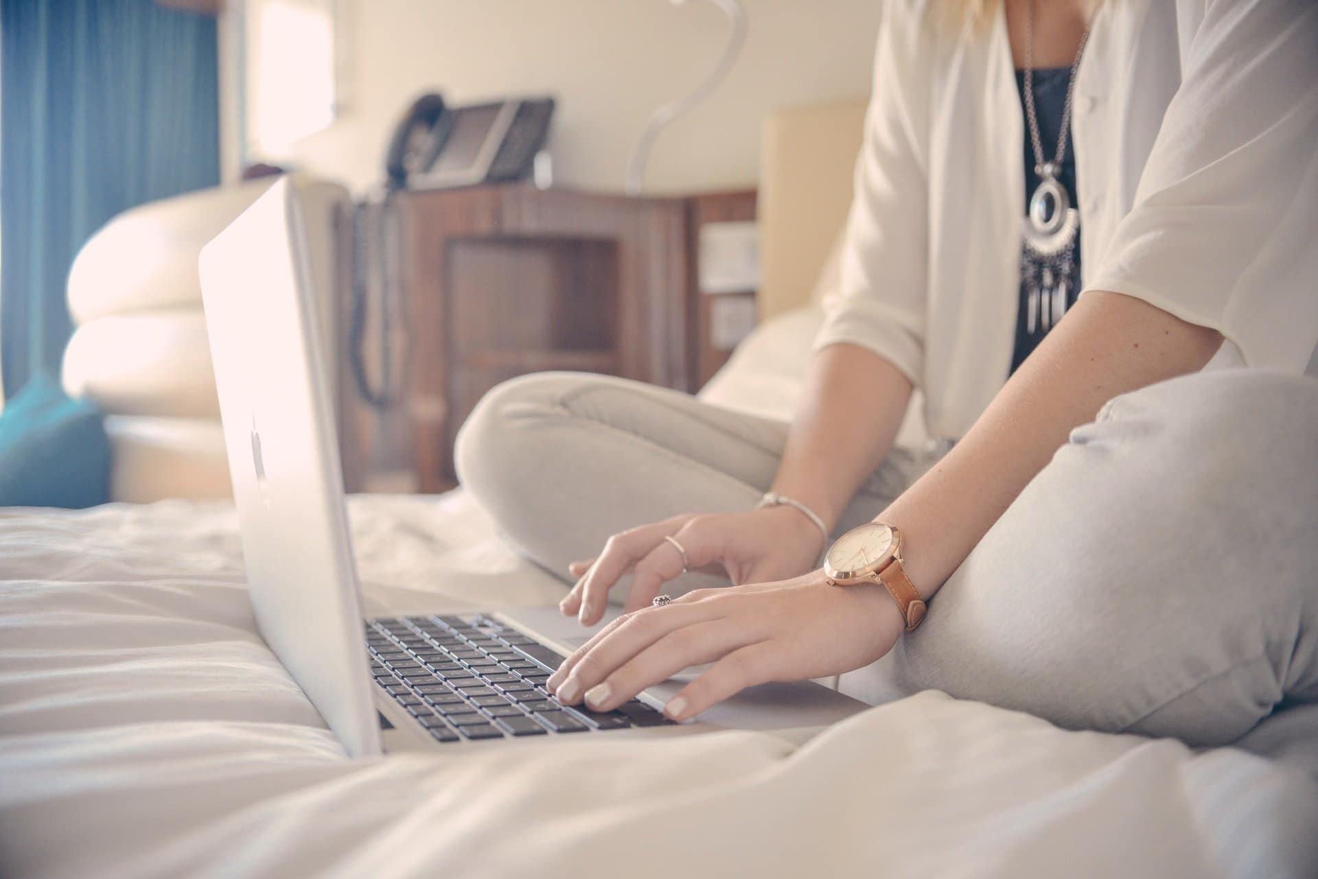Woman sitting on bed typing on a laptop